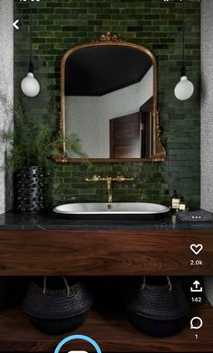 a bathroom with green brick walls and a mirror above the sink that has gold trim