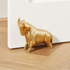 a gold rhino figurine sitting on top of a wooden floor next to a white wall