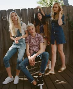 four young women and one man sitting on a chair in front of a wooden fence