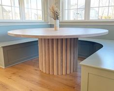 a round table in the center of a room with two benches and a vase on top