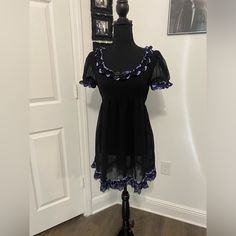 This Mini Dress Has A Non-Stretch Sheer Chiffon Construction, Two-Tone Ruffled Lace Trim, An Empire Waistline, Short Puff Sleeves With Elastic Trim, And Adjustable Ribbon Ties At The Waist. Short Sleeve Mini Dress With Ruffles For Costume Party, Short Sleeve Ruffled Mini Dress For Costume Party, Black Mini Dress With Lace Trim For Halloween, Black Gothic Mini Dress With Lace Trim, Gothic Mini Dress With Ruffles And Short Sleeves, Short Sleeve Dresses With Ruffles For Halloween, Black Lace Trim Mini Dress For Costume Party, Short Sleeve Ruffled Dresses For Halloween, Black Mini Dress With Lace Trim For Costume Party