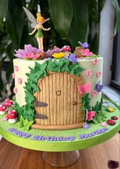 a decorated cake with a fairy door and flowers on the top is sitting on a table