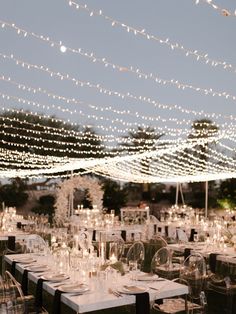 an outdoor wedding reception with clear chairs and string lights strung over the tables at night