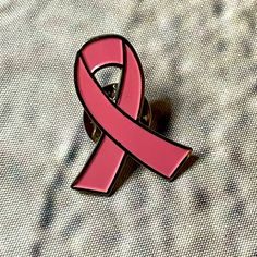 a pink ribbon pin sitting on top of a white cloth