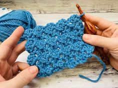 someone crocheting a piece of blue yarn on top of a wooden table with two hands