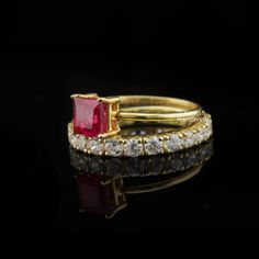 two gold rings with red and white stones on black reflective background, close up photo