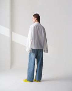 a woman standing in front of a white wall wearing blue jeans and a white shirt