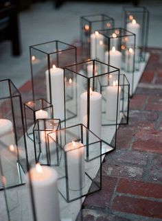 many white candles are placed in glass containers on the brick floor, along with one another