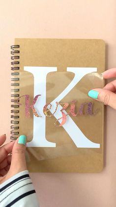 a person is holding up a sticker to the letter k in front of a notebook