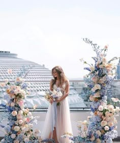 a woman standing in front of an arch with flowers and greenery on the side