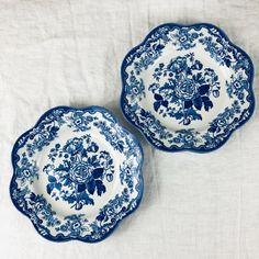 two blue and white plates sitting on top of a bed next to eachother