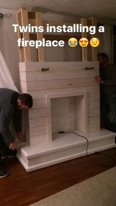 two men working on a fireplace in a living room with white walls and wood floors