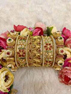 a bunch of bracelets sitting on top of a white fur covered floor next to flowers