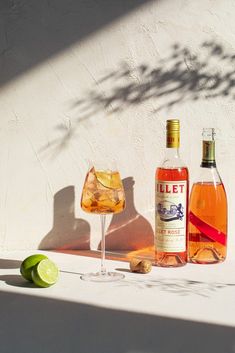 two bottles of alcohol sitting on top of a table next to a glass and lime