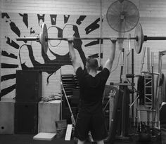 a man is lifting a barbell in a crossfit gym with graffiti on the wall behind him