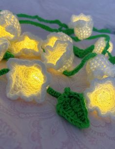 crocheted white flowers with green stems are on a tablecloth, next to a string of lights