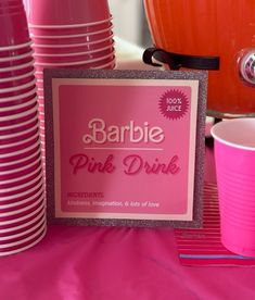 there is a pink drink sign on the table with many cups and plates around it