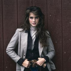 a woman standing in front of a wooden wall with her hands in her pockets and smiling