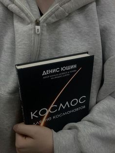 a person holding a book in their hands and wearing a hoodie with the words kosmoq written on it