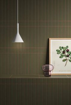 a green tiled wall with an art piece on the shelf next to it and a lamp hanging above