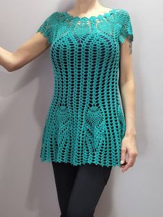 a woman wearing a green crochet top and black leggings stands in front of a gray wall