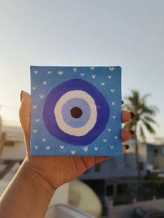 a hand holding up a blue square with white hearts on it and an eyeball in the center