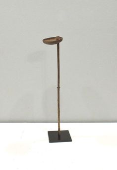 a metal pole with a wooden top on a black stand in front of a white wall