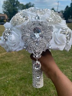 a bridal bouquet with white roses and crystal brooches is held by someone's hand