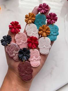 a person's hand holding several different colored and carved heart shaped brooches