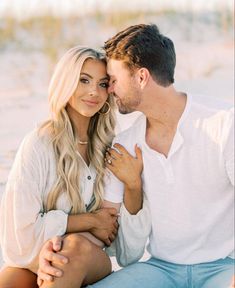 a man and woman sitting next to each other in front of the ocean with their arms around each other