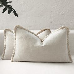 two white pillows sitting on top of a couch next to a green potted plant