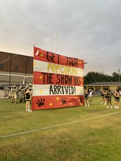 a group of cheerleaders standing in front of a large banner that reads pop corn the show has arrived