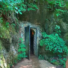 an open door in the side of a stone wall surrounded by trees and bushes with green foliage on either side