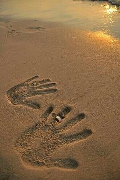 two footprints in the sand near the water at sunset or sunrise, with one person's hand and foot prints on the beach