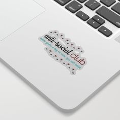 a laptop computer sitting on top of a white desk with an anti - social club sticker on the keyboard