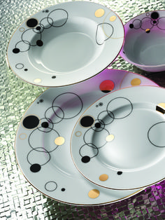 three white plates with black and gold designs on them sitting on a shiny table cloth