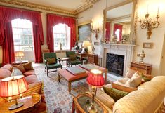 a living room filled with lots of furniture and red drapes on the windowsill