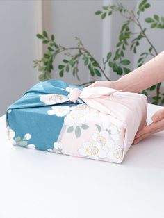 a woman opening a wrapped gift box on top of a white table next to a potted plant