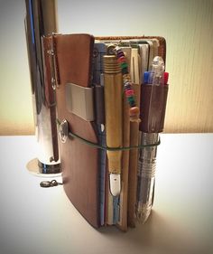 an open book with pens, pencils and other office supplies in it on a table