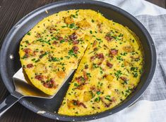 an omelet with bacon and chives in a skillet on a wooden table