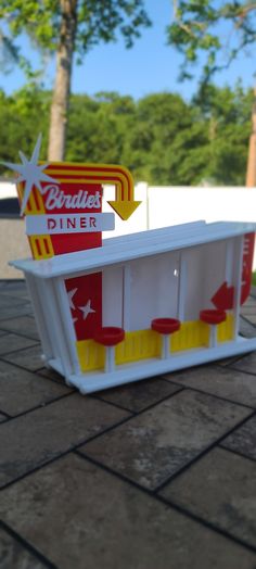 a toy model of a diner with red and yellow stools on the ground next to trees