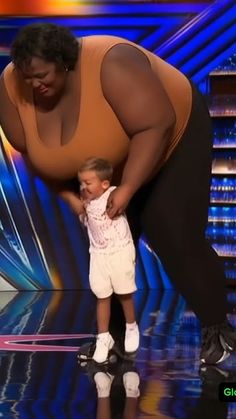 a woman standing next to a little boy on top of a stage in front of a tv screen