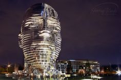 a very tall building sitting next to a body of water in the middle of a city at night