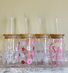 four clear glass jars with wooden lids and floral designs on the lids are lined up against a white wall