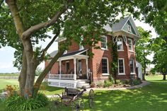 a large red brick house sitting in the middle of a lush green field next to a tree