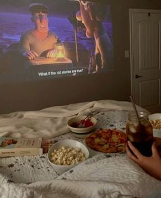 a person sitting on a bed with food and drinks in front of a movie screen