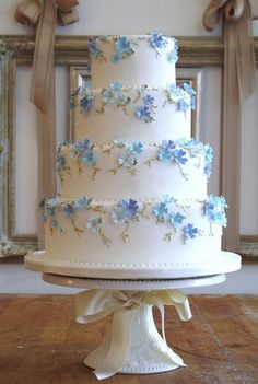 a three tiered white wedding cake with blue flowers on the top and ribbon around the edges