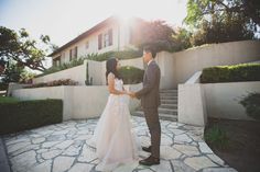 a bride and groom holding hands in front of a house with stone steps leading up to it