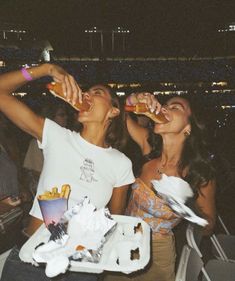 two women are drinking beer and eating food at a sporting event in an arena or stadium