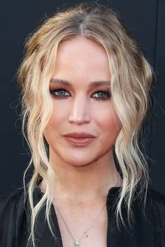 a woman with blonde hair and blue eyes is wearing a black shirt, necklace and earrings